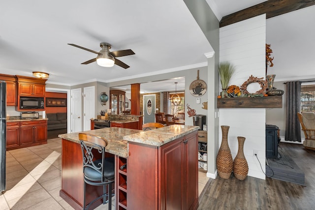 55 Trask Side Rd, Alton, NH 03810 - kitchen with black microwave, a wood stove, a kitchen island, ceiling fan, and dark brown cabinets
