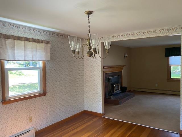 15 Vernon Ave, Rochester, NH 03867 - unfurnished dining area with a baseboard heating unit, wood finished floors, a wood stove, a chandelier, and wallpapered walls