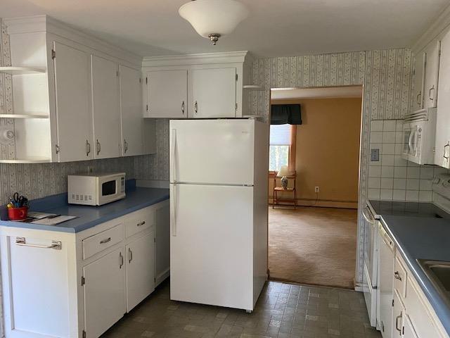 15 Vernon Ave, Rochester, NH 03867 - kitchen with white appliances, open shelves, wallpapered walls, white cabinetry, and backsplash