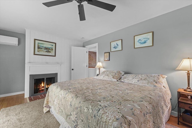 564 St Albans Rd, Swanton, VT 05488 - bedroom featuring a fireplace, a wall mounted air conditioner, wood finished floors, and a ceiling fan