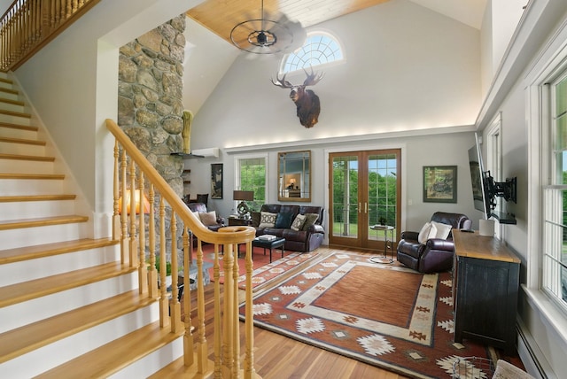 84 Shaw Rd, Northfield, NH 03276 - living room with french doors, high vaulted ceiling, wood finished floors, stairs, and a baseboard radiator