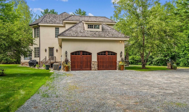 44 Buker Way, New London, NH 03257 - view of front of home with stucco siding, gravel driveway, a front lawn, stone siding, and a garage