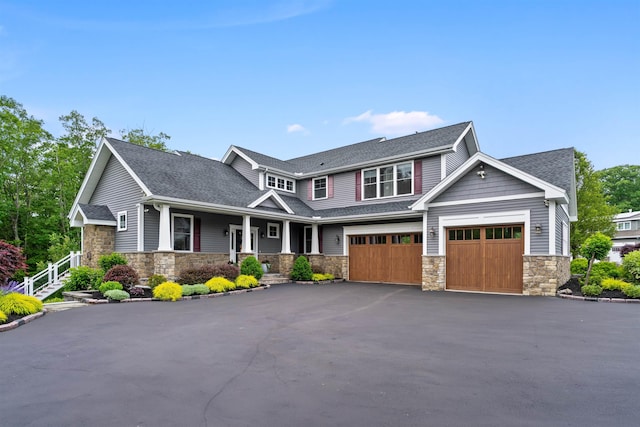 74 Childs Dr, Dover, NH 03820 - view of front of property featuring stone siding, covered porch, asphalt driveway, a garage, and roof with shingles