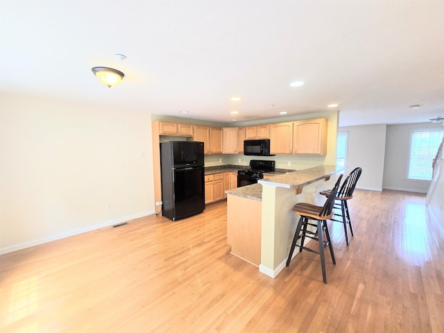 69 Mulberry St Unit 3, Concord, NH 03301 - kitchen featuring black appliances, light brown cabinetry, a peninsula, light wood-style flooring, and a breakfast bar area