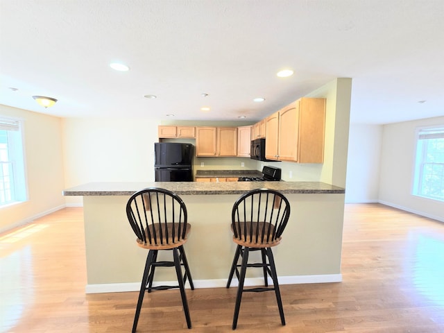 69 Mulberry St Unit 3, Concord, NH 03301 - kitchen featuring black appliances, light brown cabinetry, a peninsula, light wood-type flooring, and a breakfast bar