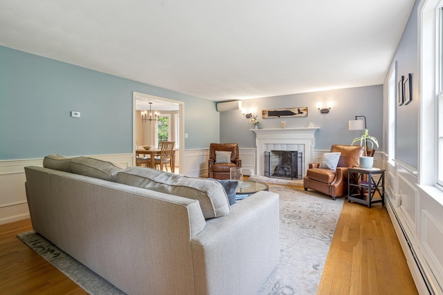 65 Forest St, Londonderry, NH 03053 - living room featuring a baseboard heating unit, a wall mounted AC, a tiled fireplace, light wood finished floors, and a wainscoted wall