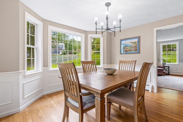 65 Forest St, Londonderry, NH 03053 - dining area with light wood-style floors, a chandelier, a wainscoted wall, a decorative wall, and a baseboard heating unit
