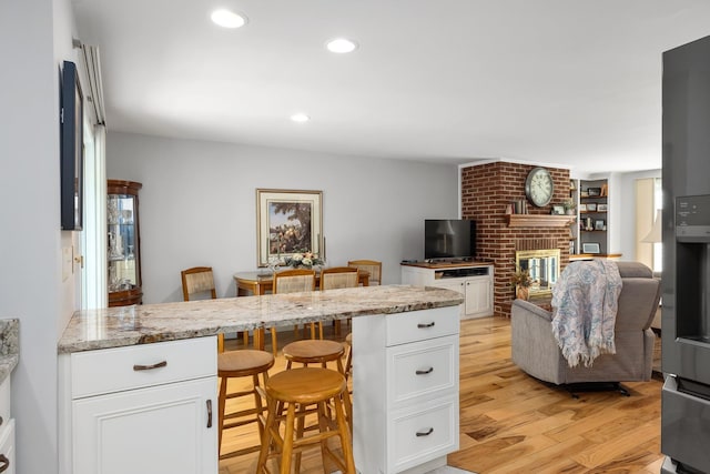 46 Pine Meadows Dr, Exeter, NH 03833 - kitchen featuring a breakfast bar, white cabinetry, light wood finished floors, a fireplace, and recessed lighting