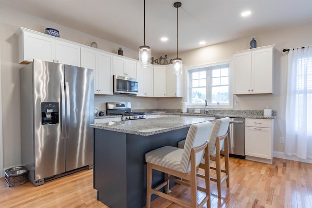 21 Catesby Ln, Londonderry, NH 03053 - kitchen featuring stainless steel appliances, a kitchen island, light wood-type flooring, white cabinets, and light stone counters