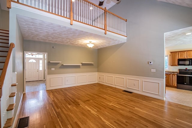 32 Saint Andrews Way, Londonderry, NH 03053 - unfurnished living room with light wood finished floors, stairway, a decorative wall, ceiling fan, and a wainscoted wall