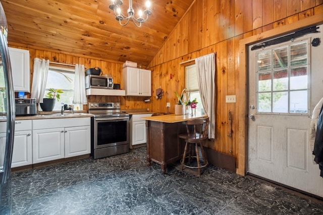 11 Providence Ave, Claremont, NH 03743 - kitchen with stainless steel appliances, vaulted ceiling, wooden walls, white cabinets, and a chandelier