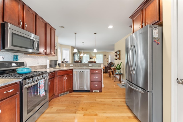 42 Leddy Dr, Epping, NH 03042 - kitchen featuring stainless steel appliances, a peninsula, light wood-style floors, decorative light fixtures, and tasteful backsplash