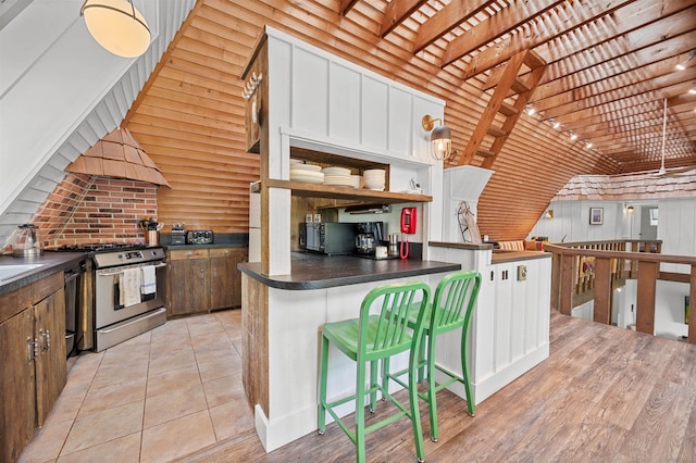 812 Airport Rd, Fayston, VT 05660 - kitchen with stainless steel gas range oven, dark countertops, a breakfast bar, open shelves, and custom range hood