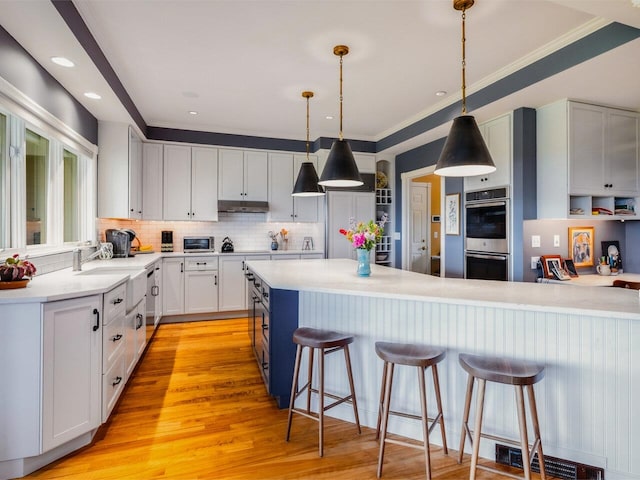 1411 Spear St, South Burlington, VT 05403 - kitchen featuring stainless steel double oven, under cabinet range hood, a kitchen breakfast bar, backsplash, and light countertops