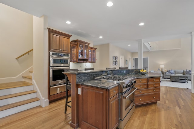4 Chablis Ct, Bedford, NH 03110 - kitchen with appliances with stainless steel finishes, a warming drawer, a kitchen bar, light wood-style flooring, and brown cabinetry