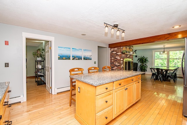33 Hillside Rd, Kingston, NH 03848 - kitchen featuring a breakfast bar area, light wood-style floors, baseboard heating, a textured ceiling, and light brown cabinetry