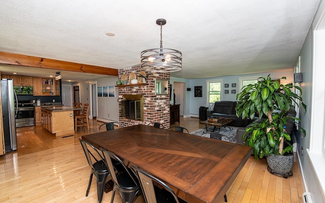 33 Hillside Rd, Kingston, NH 03848 - dining area featuring light wood-type flooring, a baseboard heating unit, a chandelier, a textured ceiling, and a fireplace