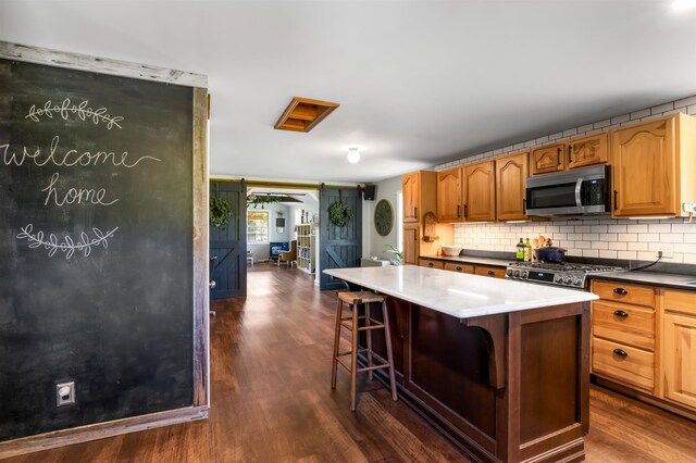 174 E Colebrook Rd, Colebrook, NH 03576 - kitchen featuring stainless steel microwave, dark wood-style flooring, tasteful backsplash, a breakfast bar area, and a center island