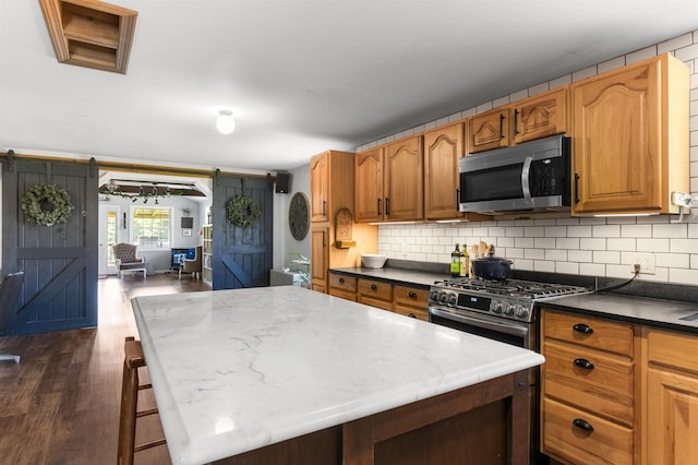 174 E Colebrook Rd, Colebrook, NH 03576 - kitchen with a barn door, appliances with stainless steel finishes, dark wood finished floors, tasteful backsplash, and a center island