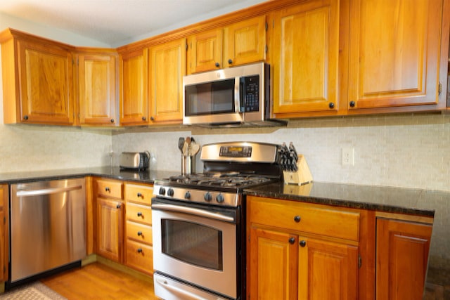 25 Benson Fuller Rd, Winhall, VT 05340 - kitchen with appliances with stainless steel finishes, brown cabinets, decorative backsplash, dark stone counters, and light wood-style flooring