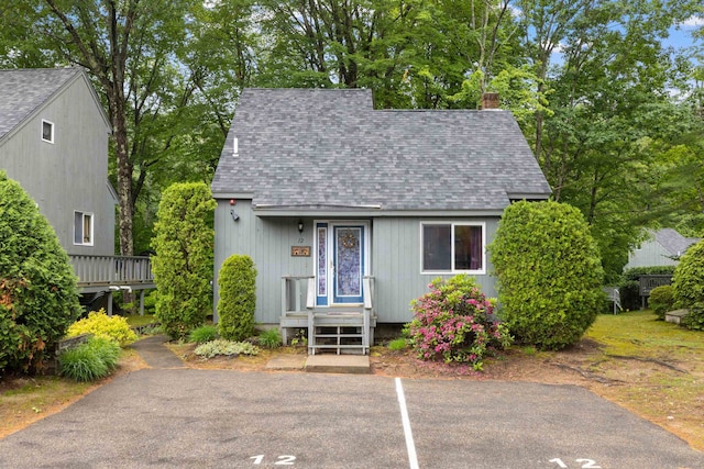 6 Cumberland Rd Unit 12, Gilford, NH 03249 - view of front of property featuring a shingled roof, uncovered parking, a chimney, and view of wooded area