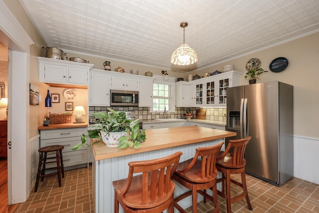 42 Lyndon St, Concord, NH 03301 - kitchen with stainless steel appliances, brick patterned floors, wainscoting, white cabinetry, and ornamental molding