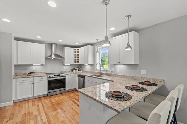 16 Daniels Dr, Lee, NH 03861 - kitchen featuring wall chimney exhaust hood, appliances with stainless steel finishes, a peninsula, light stone countertops, and white cabinetry