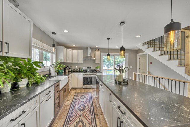 86 Chestnut St, Claremont, NH 03743 - kitchen with stainless steel range with gas stovetop, light wood-style floors, wall chimney exhaust hood, recessed lighting, and white cabinets