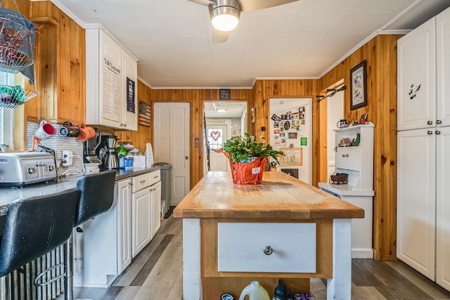 8 Myrtle St, Somersworth, NH 03878 - kitchen featuring wood finished floors, wood walls, ornamental molding, a kitchen island, and white cabinets
