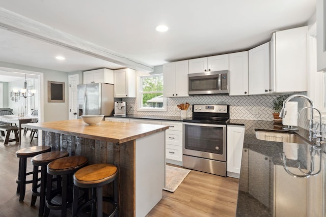 161 Micah Ter, Milton, NH 03851 - kitchen featuring appliances with stainless steel finishes, a breakfast bar, decorative backsplash, light wood-style flooring, and white cabinetry