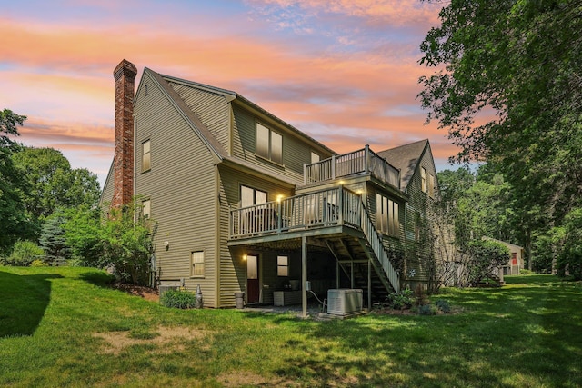 27 Olde Common Dr, Atkinson, NH 03811 - back of house at dusk with a lawn, a wooden deck, a chimney, and stairway