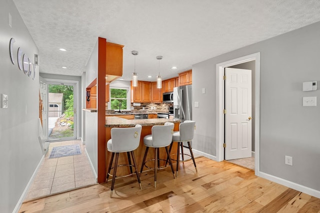56 Durham Rd Unit 62, Dover, NH 03820 - kitchen featuring appliances with stainless steel finishes, light wood-type flooring, a breakfast bar, backsplash, and brown cabinetry