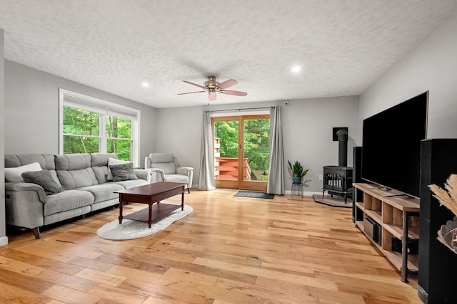56 Durham Rd Unit 62, Dover, NH 03820 - living room featuring a wood stove, a textured ceiling, a ceiling fan, light wood-style flooring, and plenty of natural light