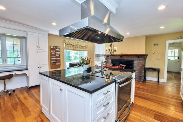 16 Storybrook Ln, Amherst, NH 03031 - kitchen featuring island exhaust hood, stainless steel range with electric stovetop, hardwood / wood-style floors, white cabinetry, and a fireplace