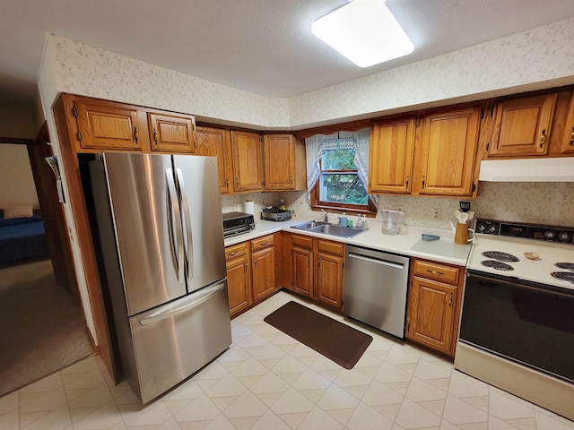 6 Cypress Ln, Essex, VT 05452 - kitchen featuring appliances with stainless steel finishes, under cabinet range hood, wallpapered walls, brown cabinetry, and light countertops