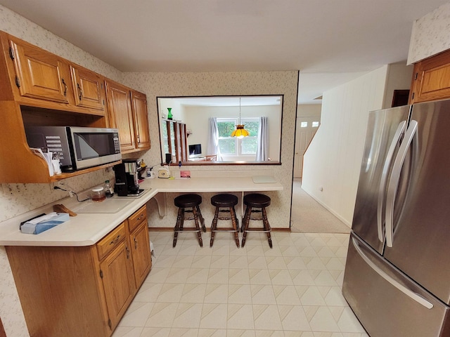 6 Cypress Ln, Essex, VT 05452 - kitchen featuring stainless steel appliances, light countertops, a breakfast bar, brown cabinets, and light flooring