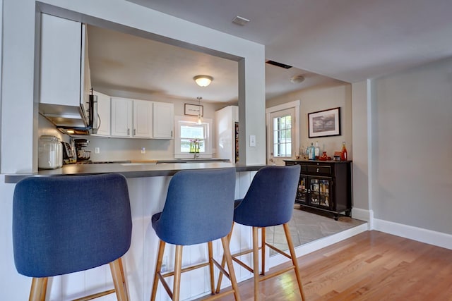15 Arbor St # 1, Exeter, NH 03833 - kitchen with a peninsula, dark countertops, light wood finished floors, a breakfast bar, and white cabinets