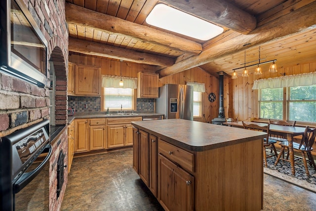 572 Old Cheshire Tpke, Charlestown, NH 03603 - kitchen with appliances with stainless steel finishes, a wood stove, dark countertops, a wooden ceiling with exposed beams, and a center island