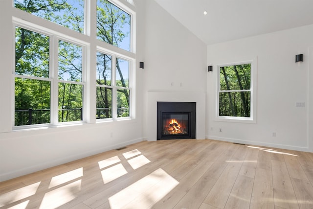 74 Scenic View Rd, Ashland, NH 03217 - unfurnished living room with high vaulted ceiling, plenty of natural light, a glass covered fireplace, and light wood-style floors