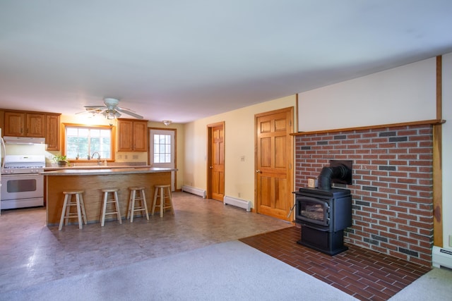 144 Packers Falls Rd, Durham, NH 03824 - kitchen with white range with gas cooktop, under cabinet range hood, baseboard heating, a breakfast bar area, and a wood stove