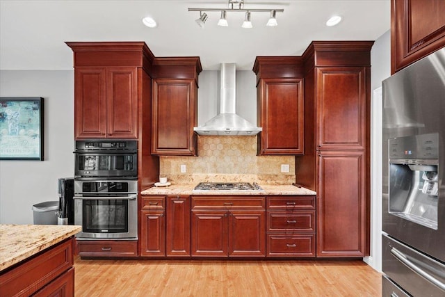 23 Surrey Ln, Laconia, NH 03246 - kitchen featuring appliances with stainless steel finishes, wall chimney range hood, backsplash, dark brown cabinets, and light wood-type flooring