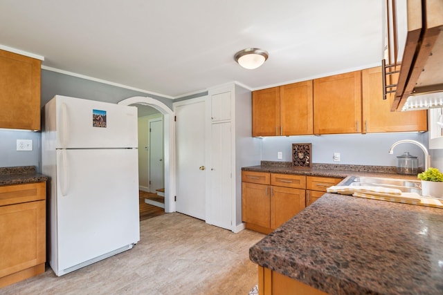 626 County Rd, New London, NH 03257 - kitchen with freestanding refrigerator, brown cabinetry, arched walkways, dark stone counters, and ornamental molding