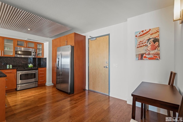 255 N Sierra St Unit 2013, Reno, NV 89501 - kitchen with stainless steel appliances, dark wood-style floors, glass insert cabinets, backsplash, and brown cabinetry