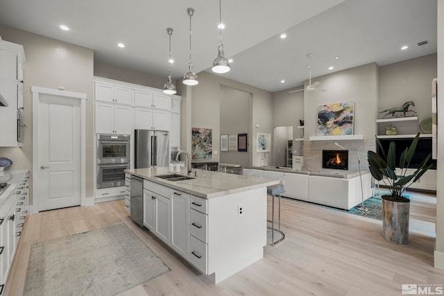 718 W Pleasant Oak Trl, Reno, NV 89511 - kitchen with a sink, appliances with stainless steel finishes, light wood-style floors, a tiled fireplace, and a towering ceiling