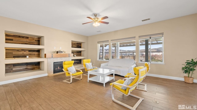 11725 Paradise View Dr, Sparks, NV 89441 - living area featuring built in shelves, baseboards, a tiled fireplace, a ceiling fan, and wood finished floors