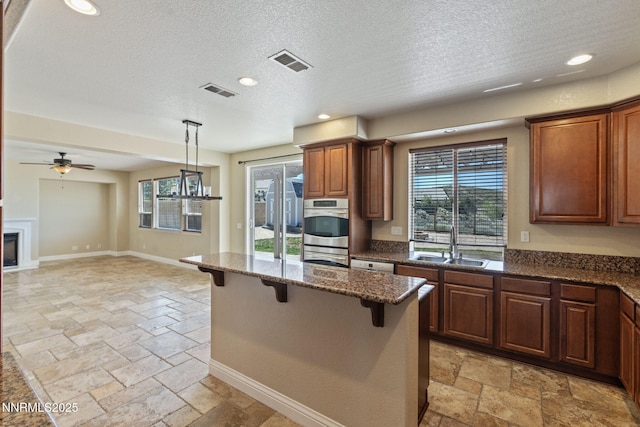 8389 Opal Ranch Way, Reno, NV 89506 - kitchen with a sink, stone tile floors, a breakfast bar area, double oven, and dark stone countertops