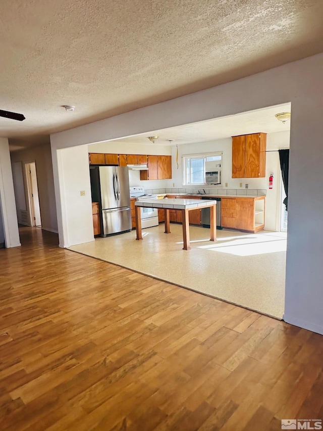 815 16th St, Lovelock, NV 89419 - kitchen featuring appliances with stainless steel finishes, tile counters, brown cabinetry, a textured ceiling, and light wood finished floors