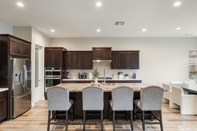 kitchen with stainless steel appliances, light wood-style floors, dark brown cabinetry, a breakfast bar area, and recessed lighting