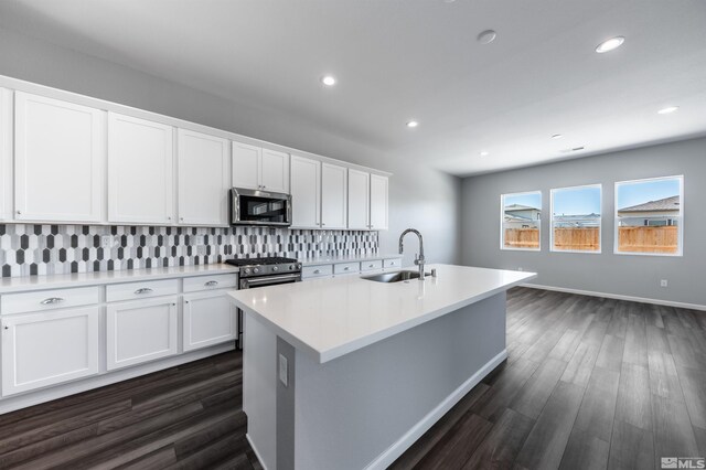 kitchen featuring a sink, appliances with stainless steel finishes, decorative backsplash, white cabinets, and a center island with sink