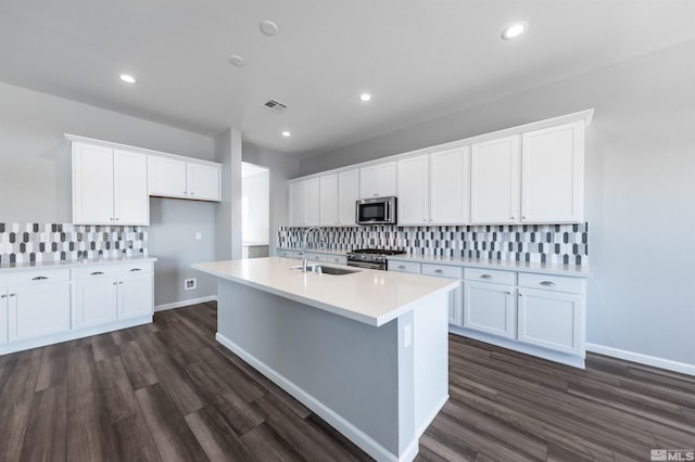 kitchen featuring stainless steel appliances, a sink, backsplash, a center island with sink, and white cabinets